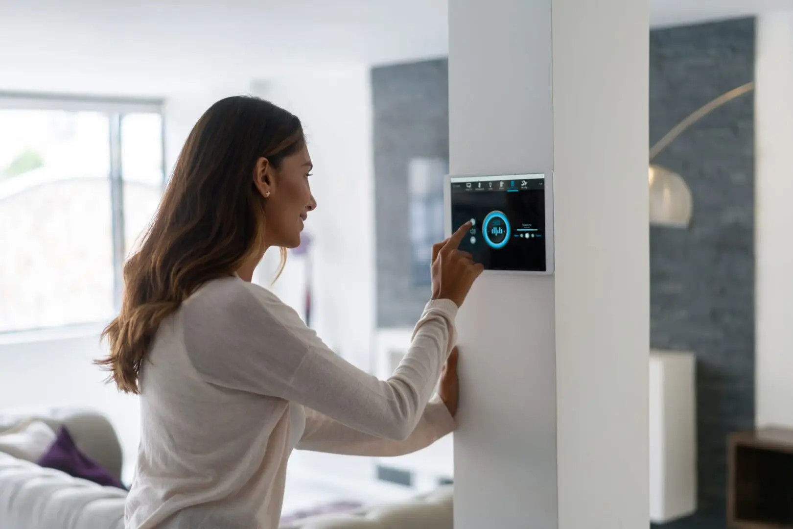 Woman adjusting a smart thermostat on a wall.