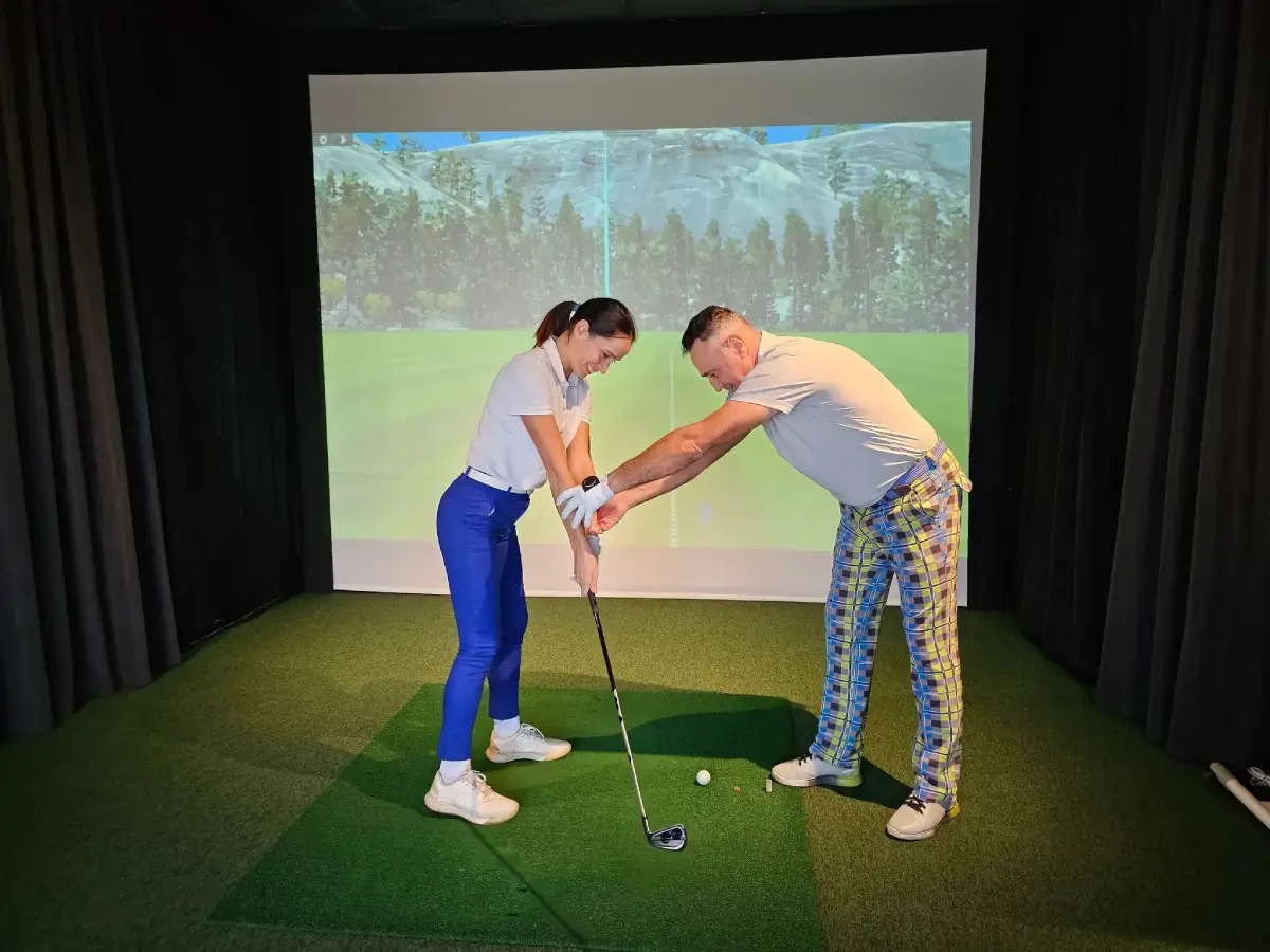 Golf instructor teaching woman in indoor simulator.