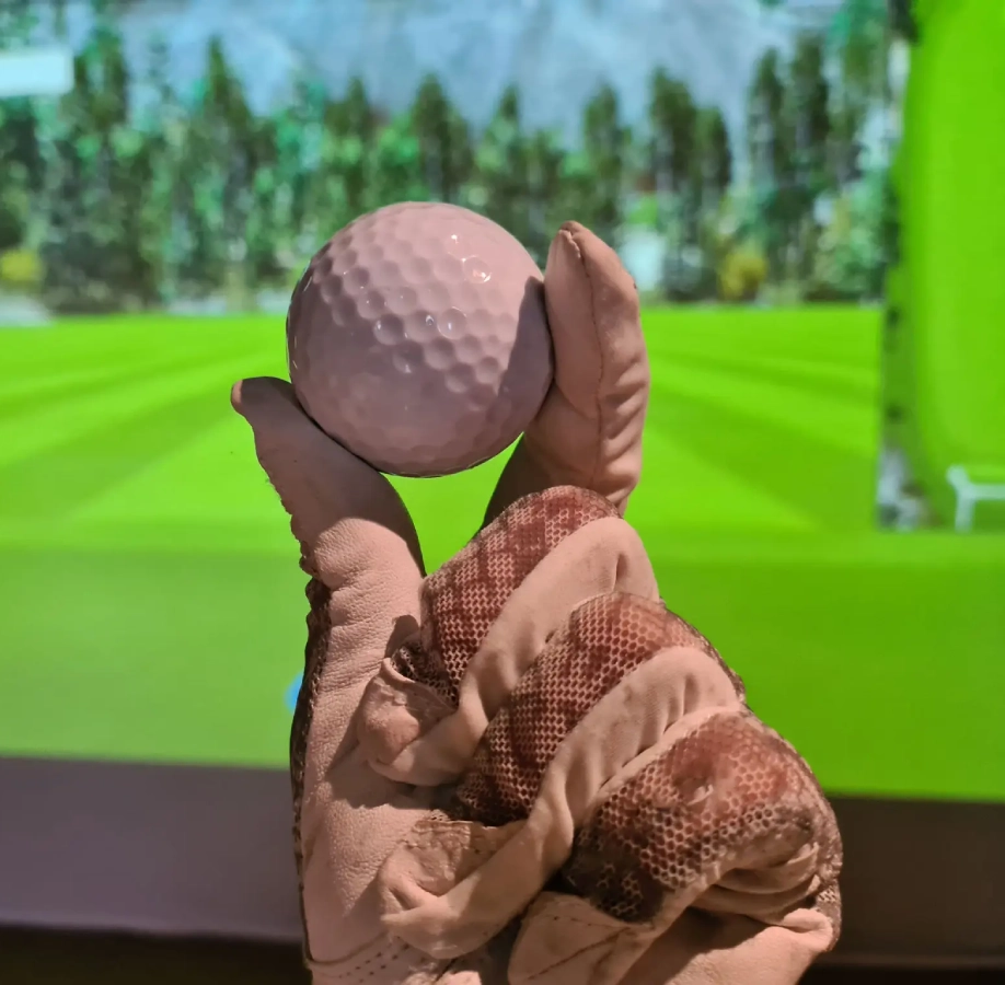 Gloved hand holding golf ball indoors.