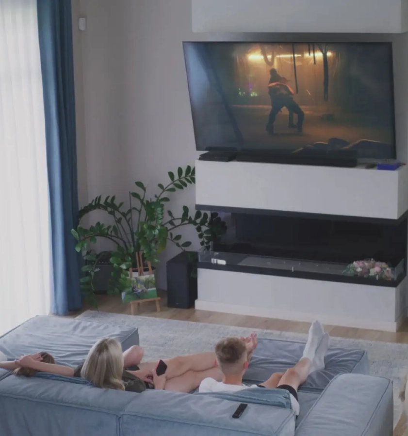 Couple watching TV on living room sofa.